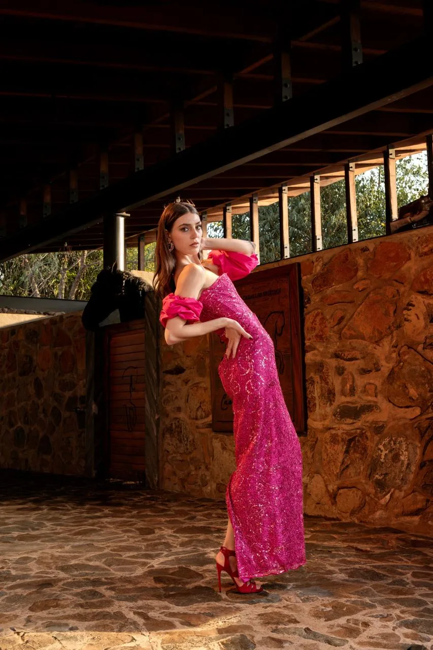 Modelo con vestido fucsia recargada en la puerta de madera de una caballeriza de piedra