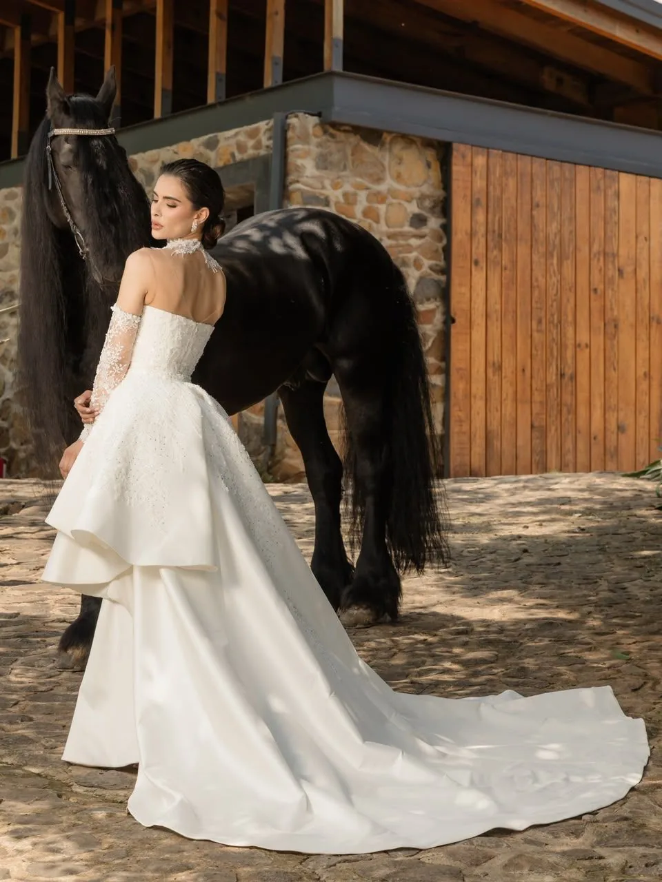Novia de espaldas con un Friesian en el empedrado del rancho